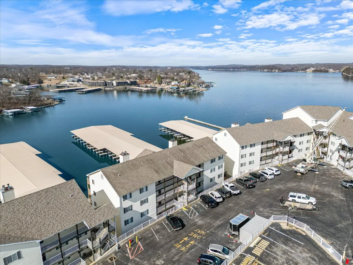 A tranquil lakeside view featuring boathouses, calm water, and nearby residential buildings. The scene offers a sense of leisure with the opportunity for fishing, boating, and picnicking by the water.