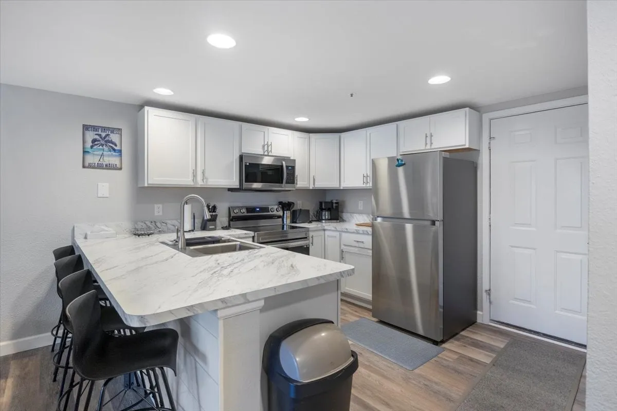 A welcoming, functional kitchen with marble countertops, stainless steel appliances, and bar stools. The scene hints at ongoing cooking or socializing activities, with an open and spacious layout that accommodates hosting.