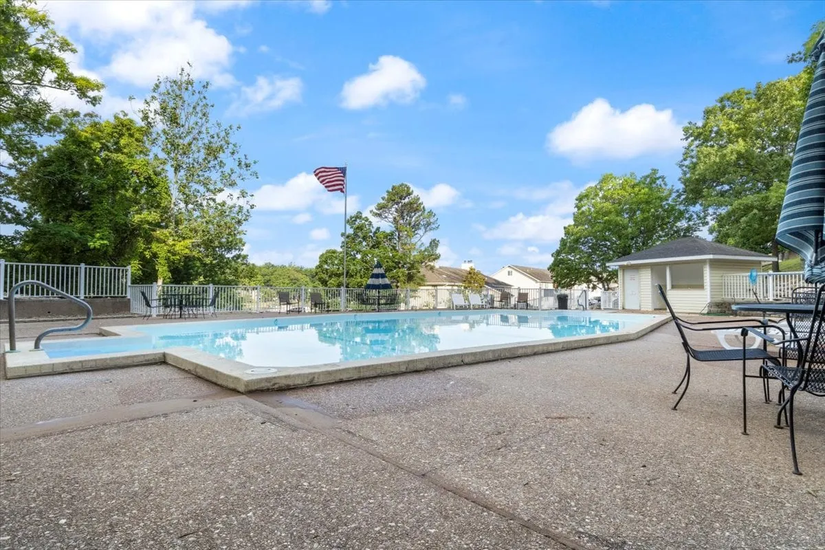 An outdoor swimming pool set amidst lush greenery, with an American flag waving and plenty of comfortable seating for families to gather and socialize. The inviting poolside area captures the essence of resort-style amenities.