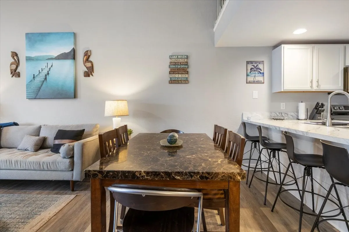 A welcoming communal space featuring a marble-top dining table, a comfortable sofa with plush cushions, and artistic wall decor. The arrangement suggests an area ideal for shared meals, board games, or relaxed conversation, with warm lighting enhancing the inviting mood.