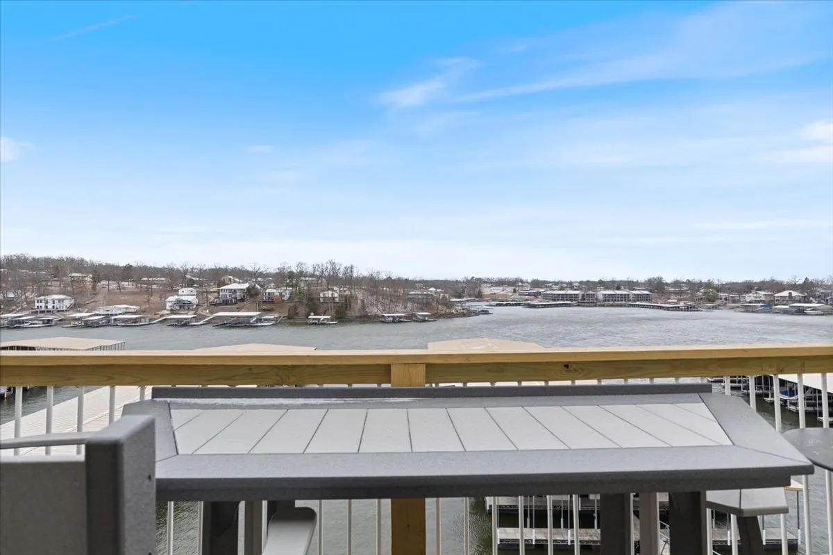 A tranquil waterfront view featuring sparkling lake water, residential houses in the distance, and a dock inviting visitors to enjoy boating and fishing. The open vista hints at opportunities for outdoor dining or relaxing as the sun rises or sets over the water.