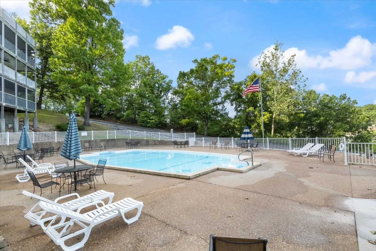 A sparkling swimming pool surrounded by lounge chairs and green trees, inviting guests to relax, swim, or gather for casual sun-filled afternoons. The American flag and verdant landscaping suggest a festive and communal atmosphere.