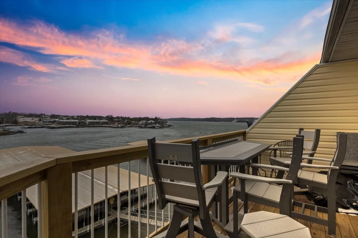 A serene outdoor seating area overlooks the lake, with comfortable chairs perfectly positioned to take in expansive water views beneath a sunset sky. The space radiates relaxation and the promise of memorable mornings with coffee or evenings with drinks.